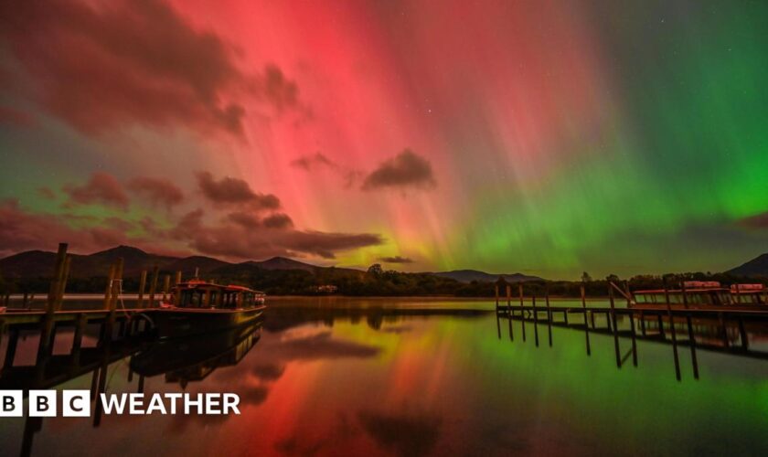 Sky filled with green and purple of the aurora with some shafts of white light running vertically. In the distance a ruined castle sits on top of a hill